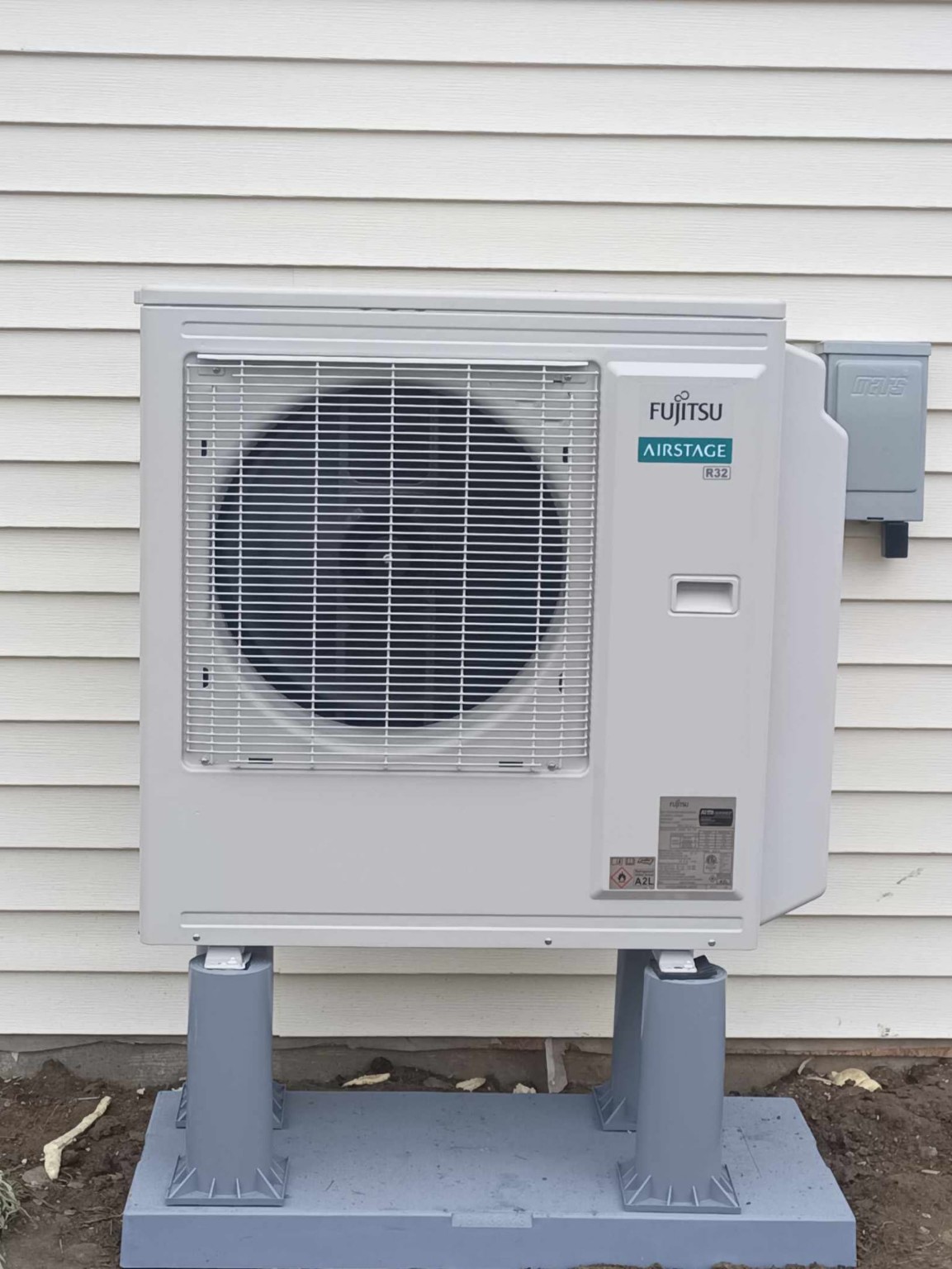Fujitsu Airstage R32 heat pump installed on a pad with risers and electrical disconnect